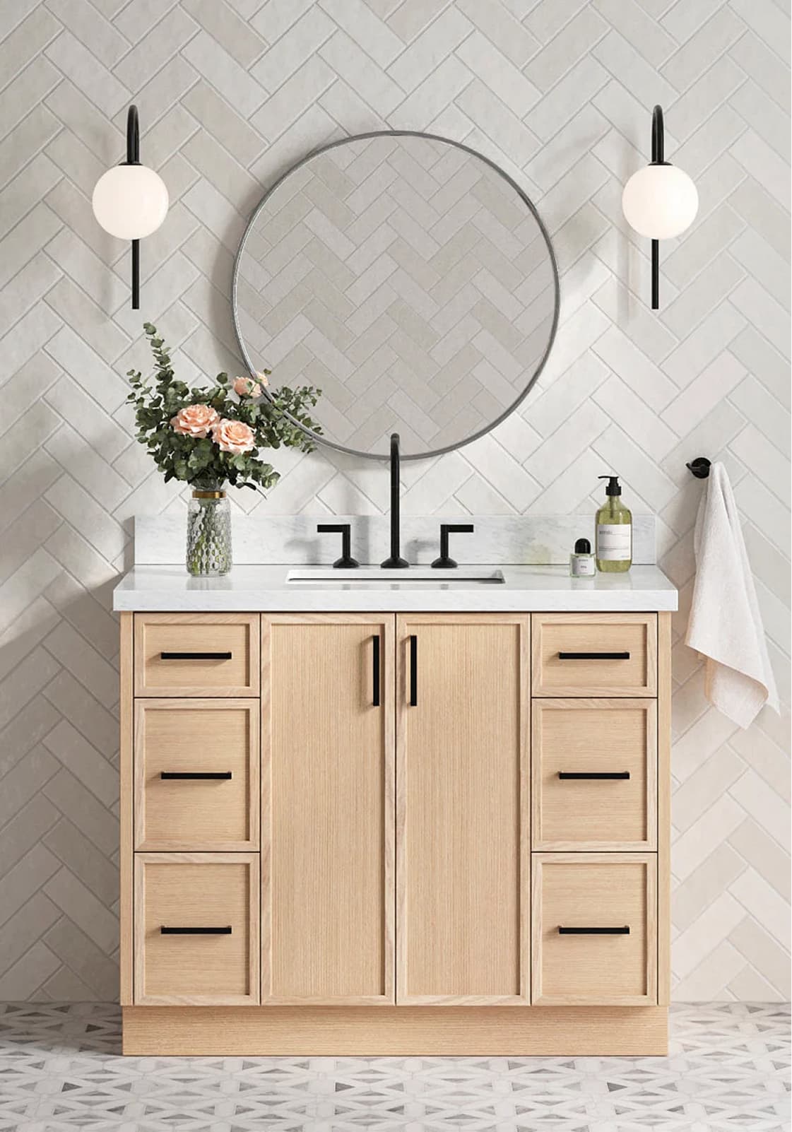 White oak bathroom vanity Light oak vanity with black hardware, round mirror, marble top, and floral decor styled against herringbone tile.